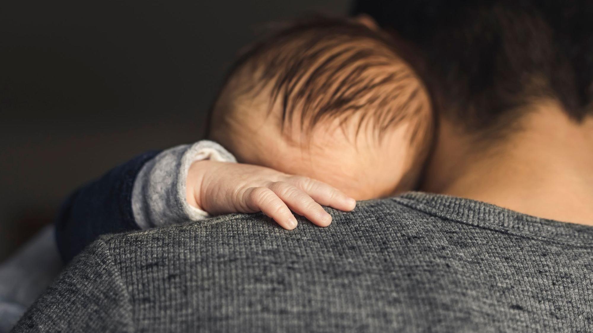 Ein Baby hat die Hand auf die Schulter des Vaters gelegt.
