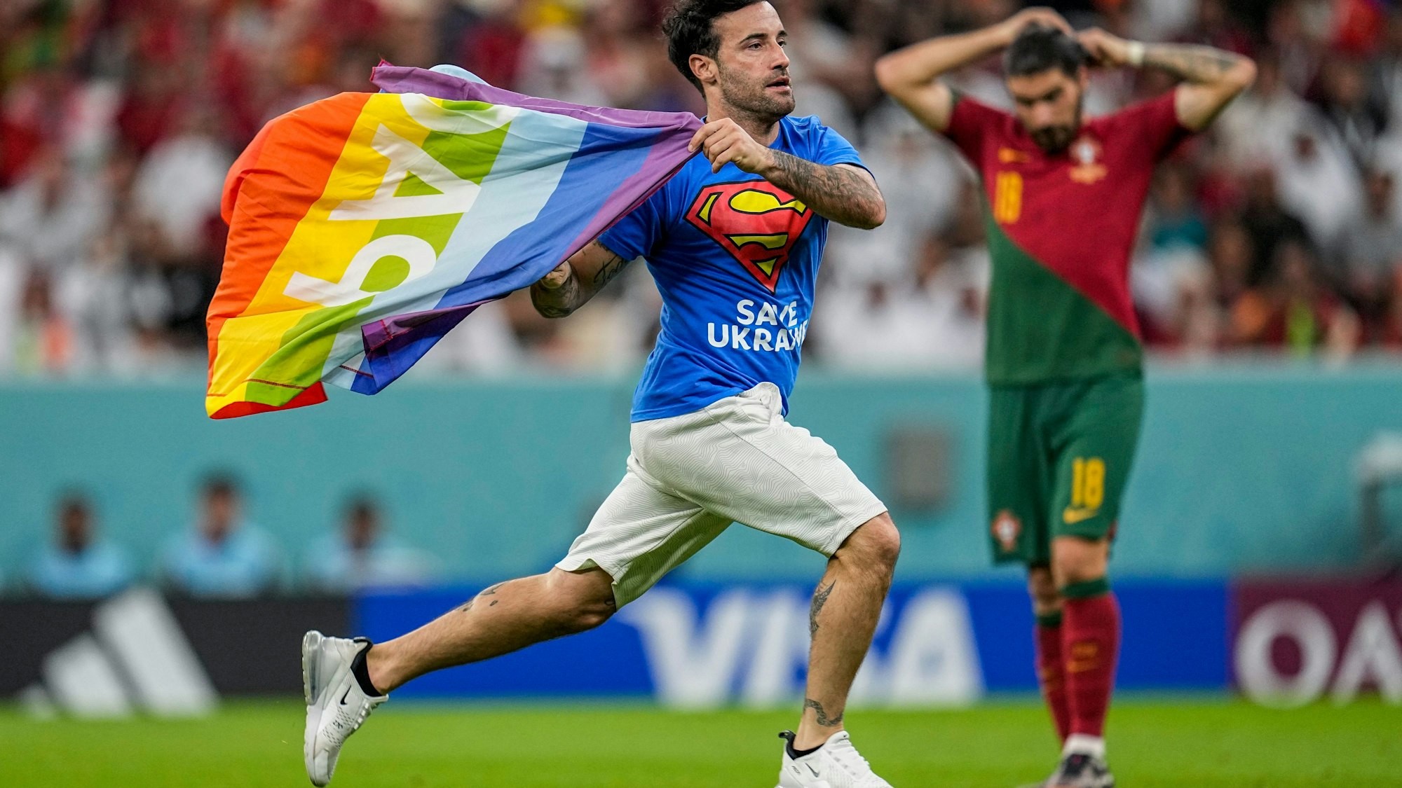 Der Italiener Marco Ferri läuft über den Rasen des Lusail-Stadions und zeigt die Regenbogenfahne. Auf seinem T-Shirt ist zu lesen: „Save Ukraine“.