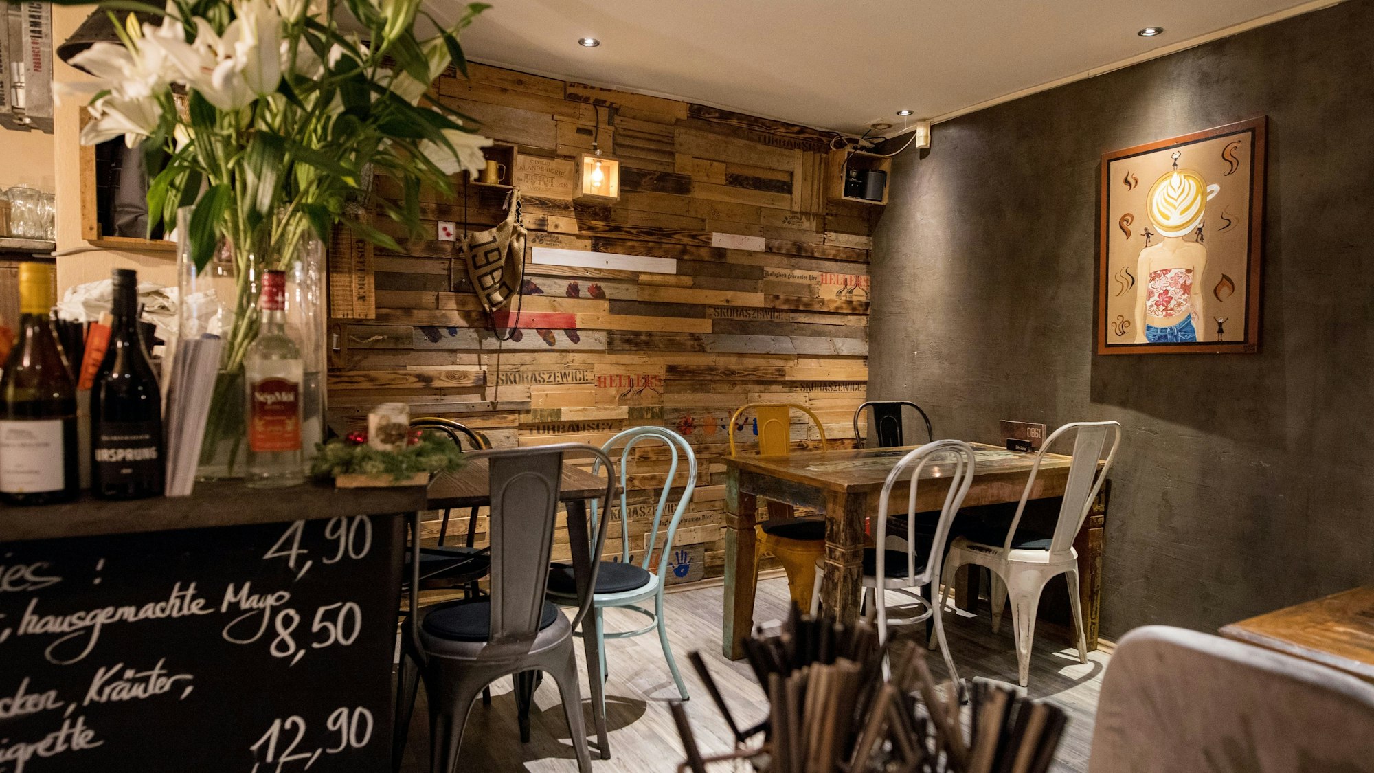 Die Inneneinrichtung des Café 1980, eine bunte Holzwand und einige Tische mit schlichten Stühlen sind zu sehen.