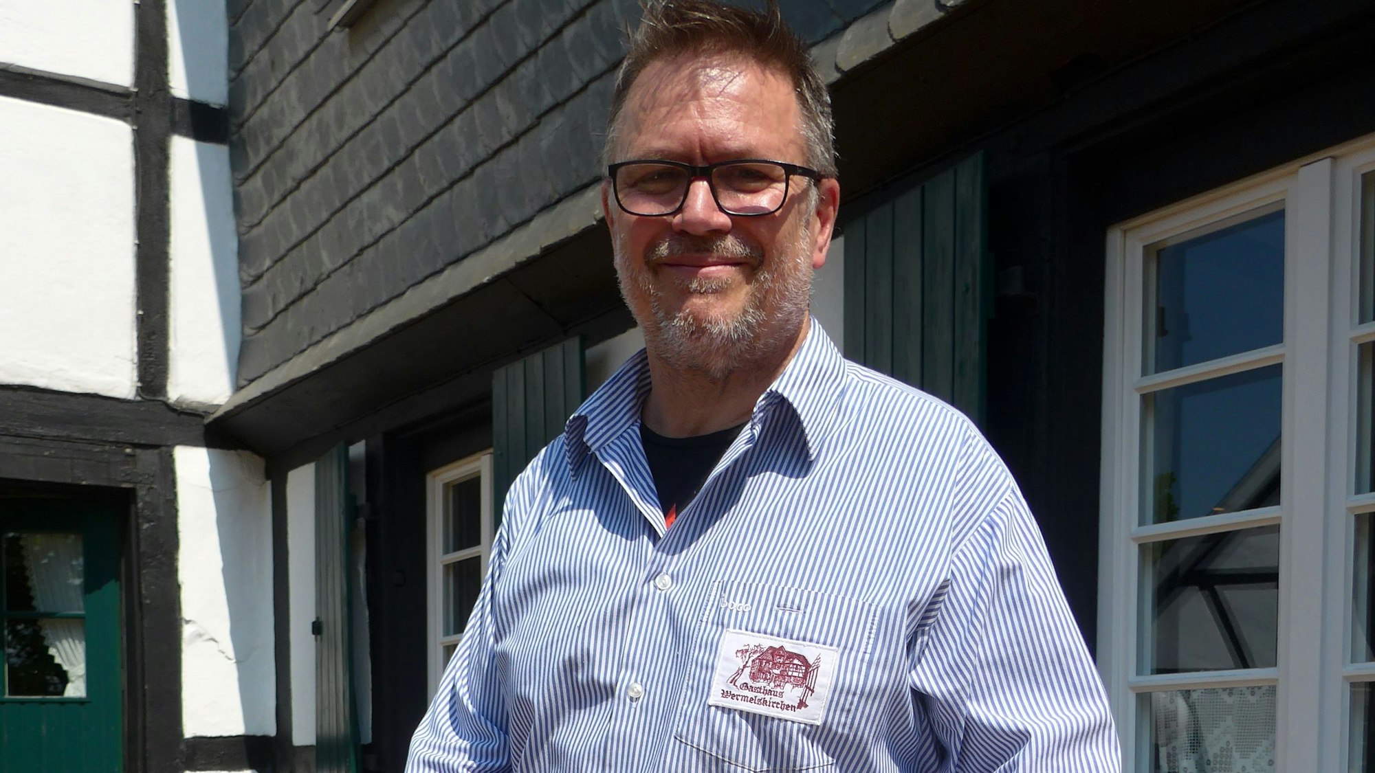 .Udo Wermelskirchen vom Gasthaus Wermelskirchen steht im blau-weß gestreiften Hemd in seinem Biergarten.