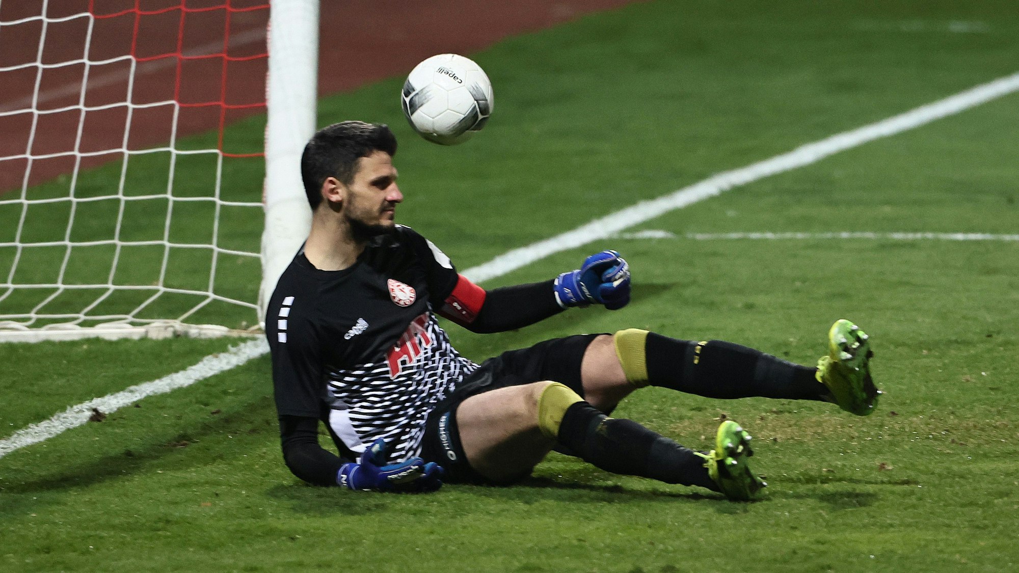 Ein Torwart sitzt auf dem Boden, der Ball ist rechts neben ihm zu sehen.