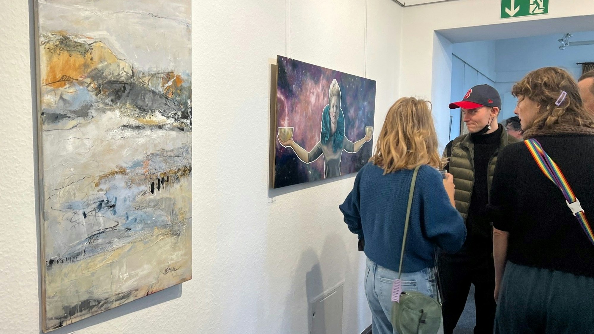 Zwei Kunstwerke hängen an der Wand im Leichlinger Bürgerhaus. Rechts stehen Besucher der Jahresaustellung.