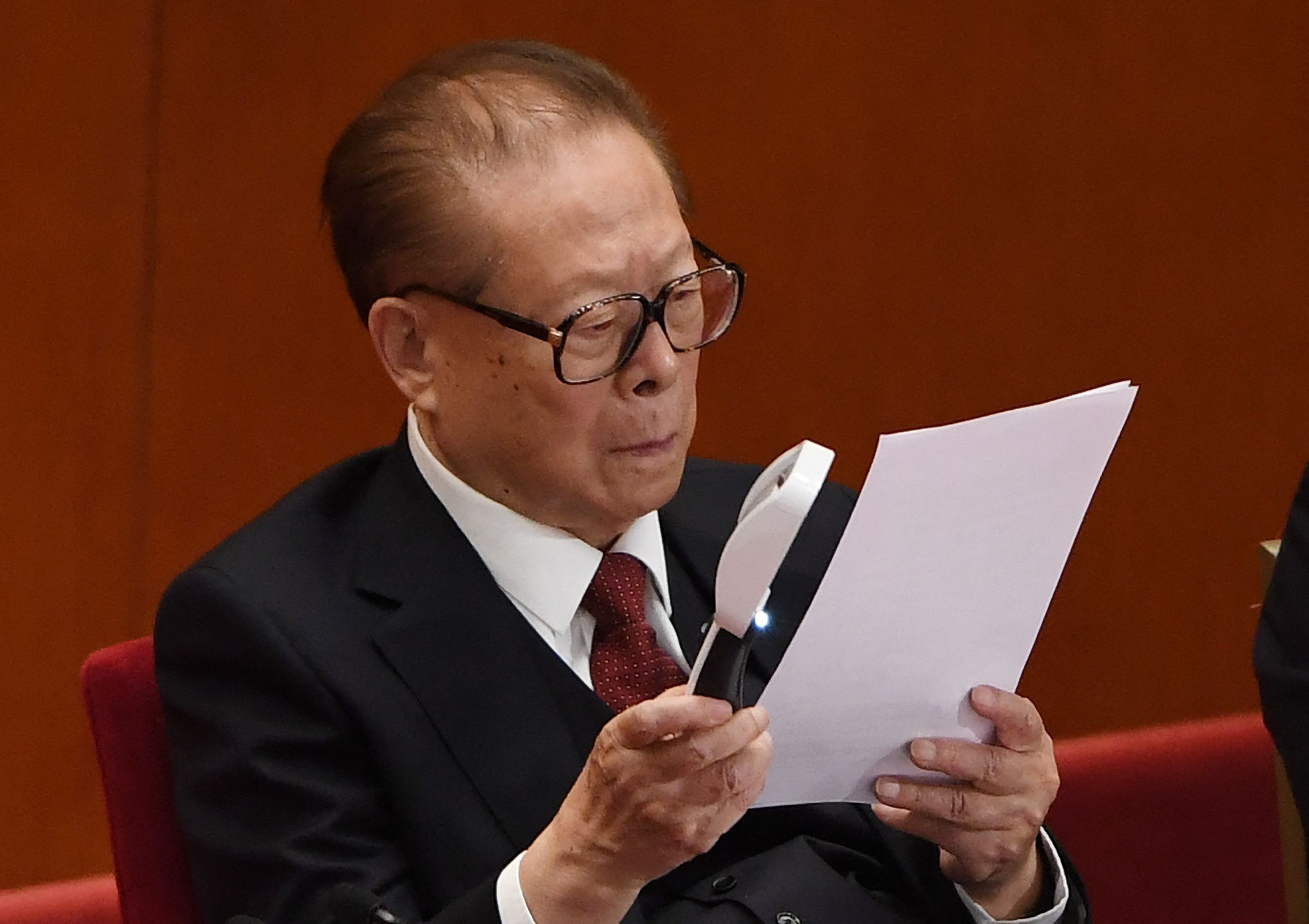 Der frühere chinesische Präsident, Jiang Zemin, liest auf einem Parteitag einen Bericht mithilfe einer Lupe.