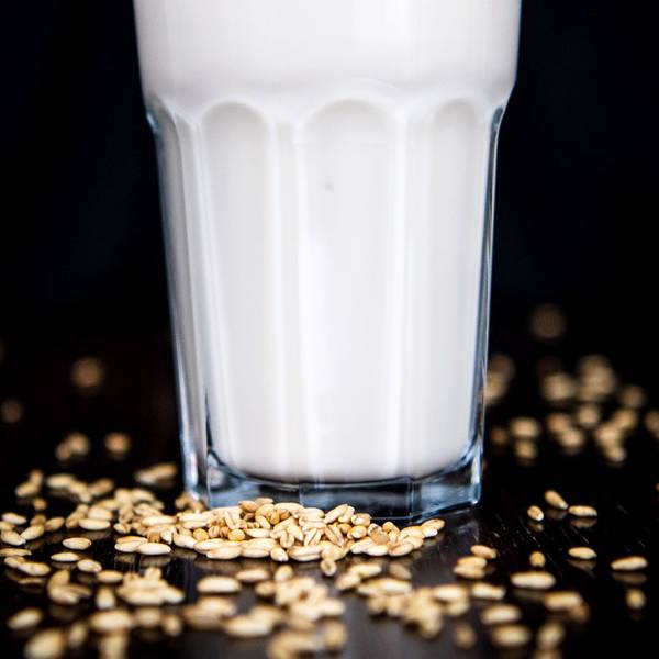 Hafermilch wird in ein Glas geschüttet. Die weiße Milch schäumt beim Kippen leicht und spritzt über den Glasrand hinaus. (Symbolbild)