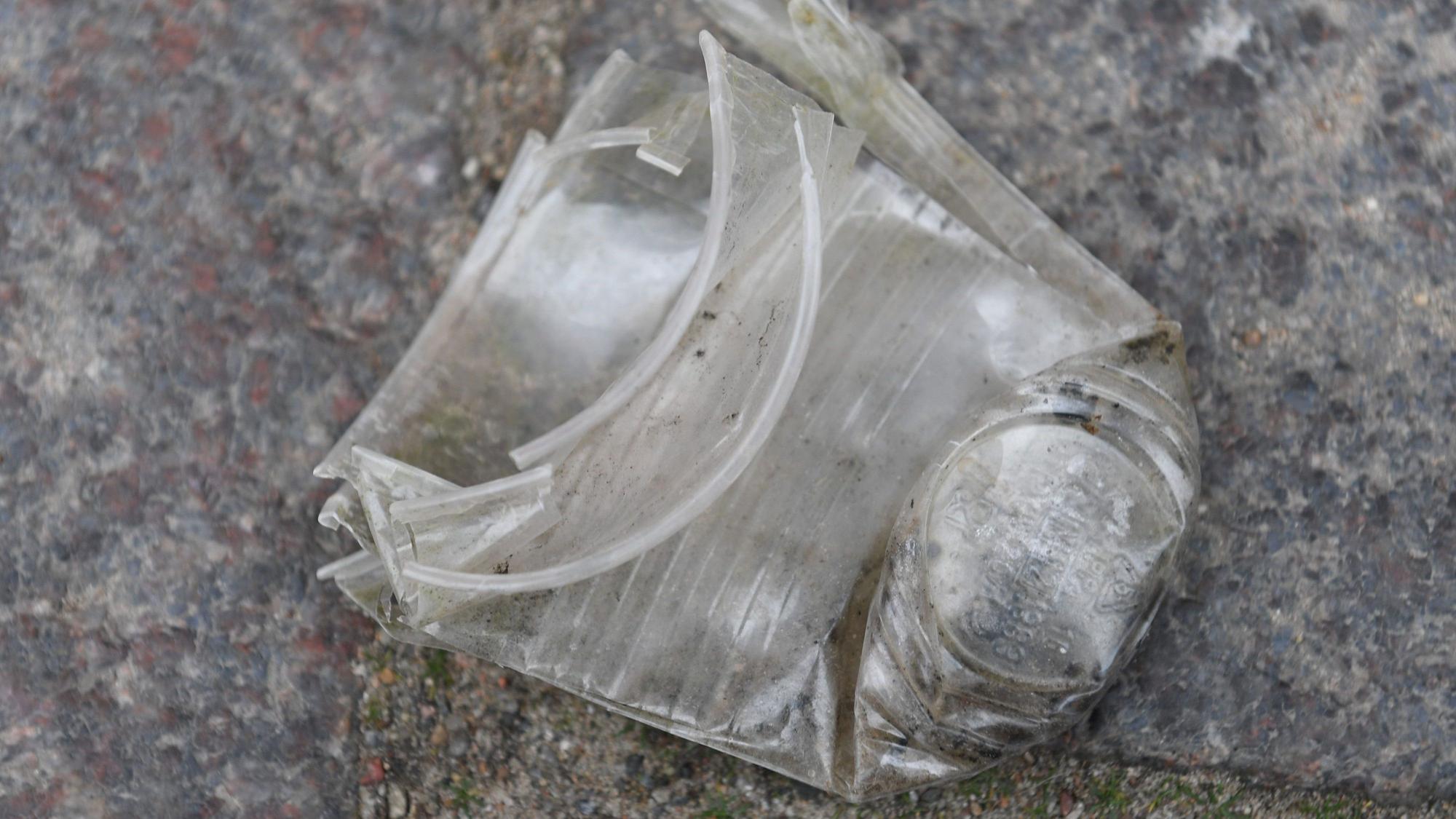 Ein zerknüllter und dreckiger Plastikbecher liegt auf einer Straße.