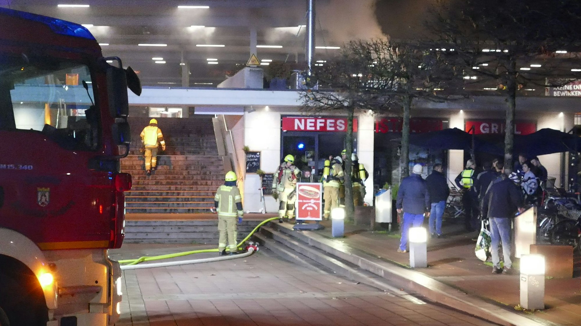 Mehrere Feuerwehrleute stehen vor einem Imbiss. Ein Feuerwehrmann geht die Treppen zum Bahnhof hoch.