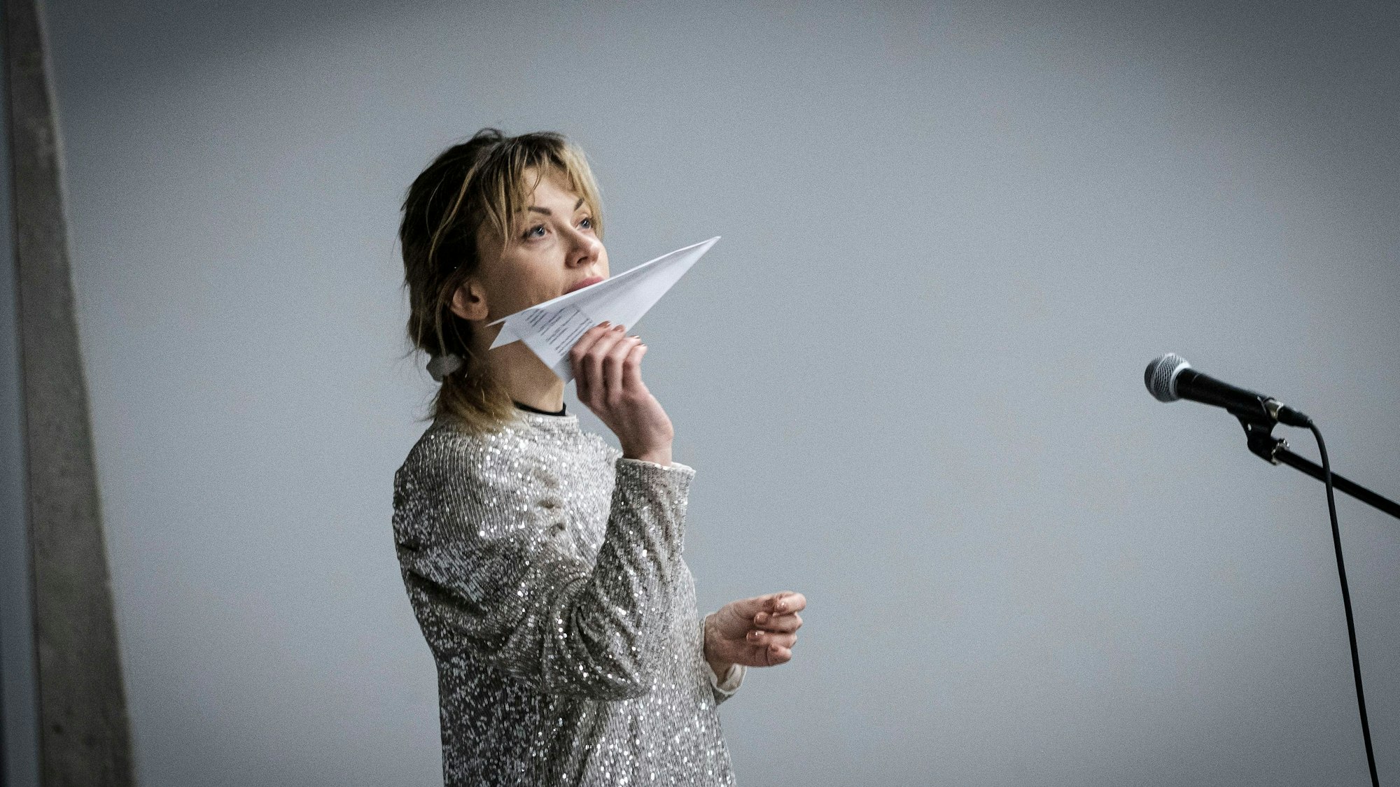 Die Schauspielerin Tetiana Zigura hält einen Papierflieger in der Hand und blickt nach oben.