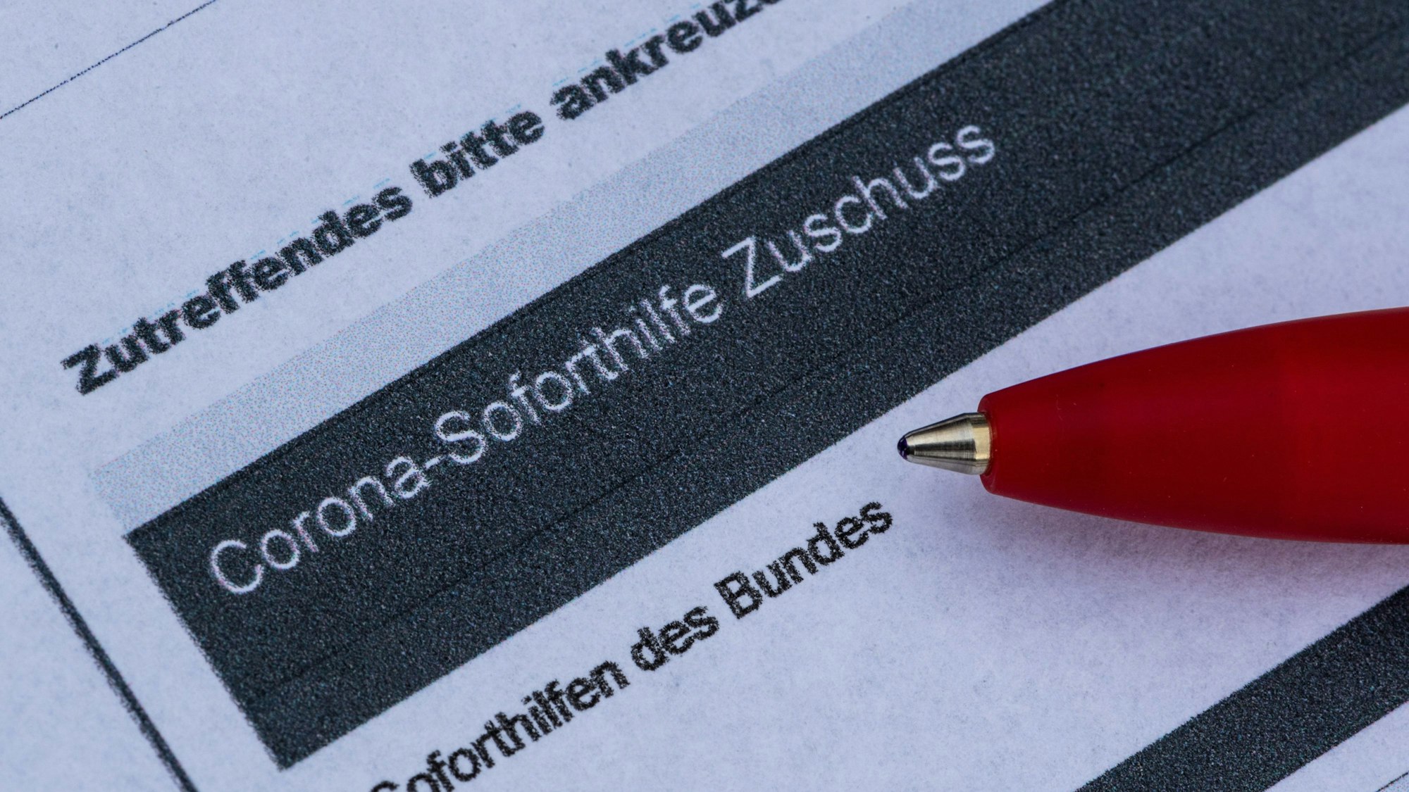 Ein Stift liegt auf einem Antrag für den Corona-Soforthilfe-Zuschuss.