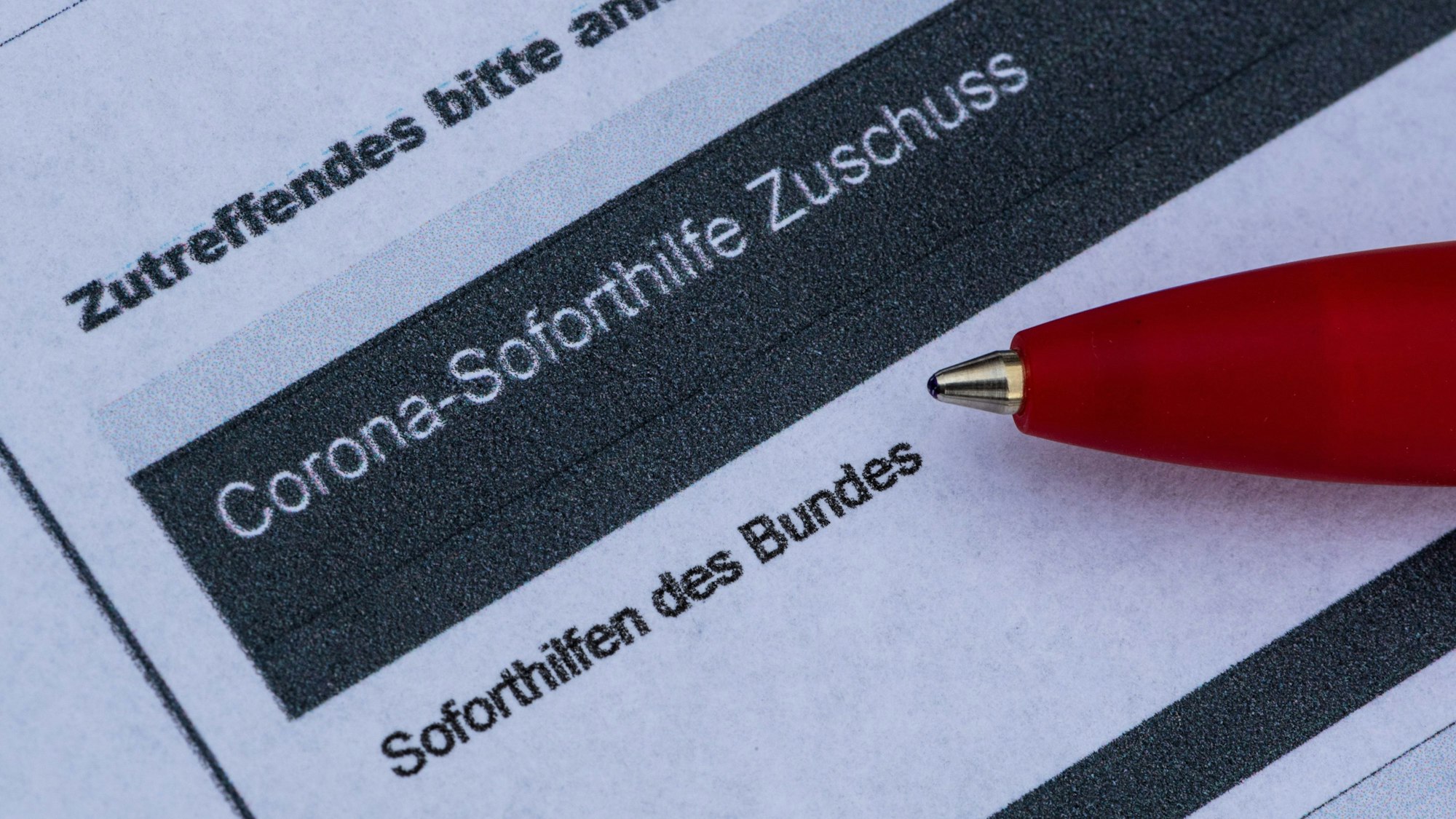 Ein Stift liegt auf einem Antrag für den Corona-Soforthilfe-Zuschuss.