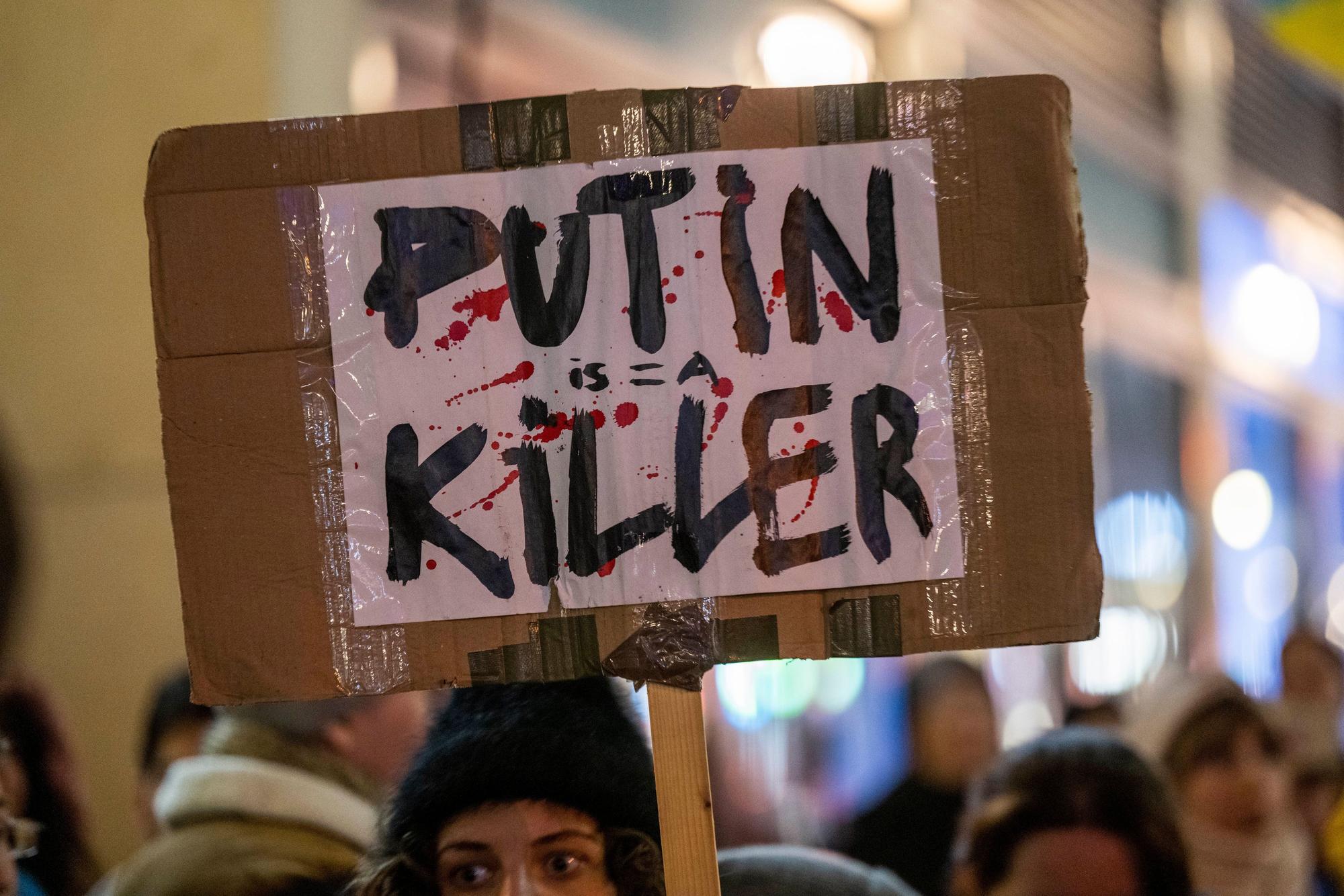 Vor dem Russischen Haus der Wissenschaft und Kultur in Berlin hält eine Demonstrantin ein mit roten Farbtropfen bespritztes Plakat mit der Aufschrift „Putin is a Killer·“ (Putin ist ein Mörder) hoch
