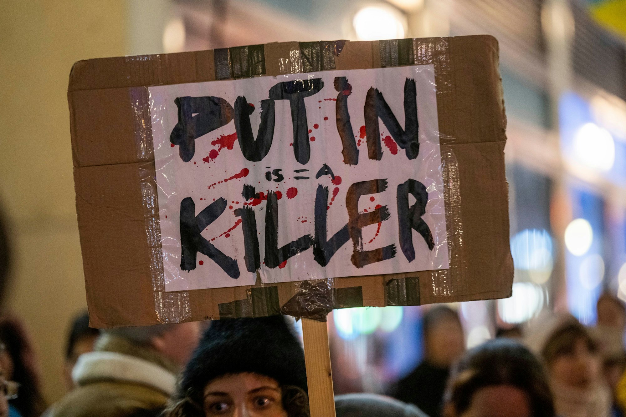 Vor dem Russischen Haus der Wissenschaft und Kultur in Berlin hält eine Demonstrantin ein mit roten Farbtropfen bespritztes Plakat mit der Aufschrift „Putin is a Killer·“ (Putin ist ein Mörder) hoch
