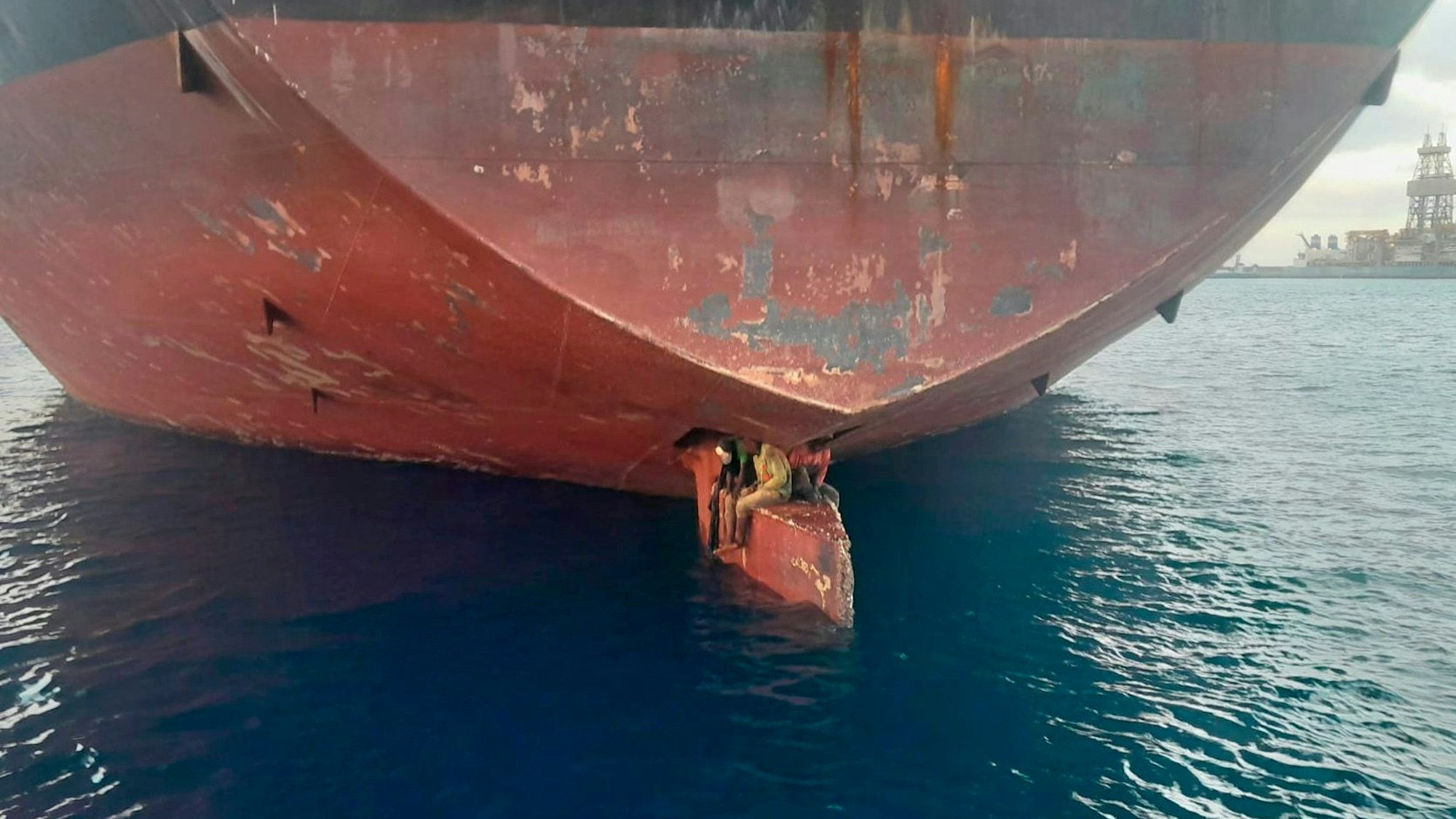 Spanien, Las Palmas: Drei Männer sitzen an einer ungewöhnlichen und gefährlichen Stelle eines Öltankers, der in einem Hafen der Kanarischen Inseln vor Anker liegt.