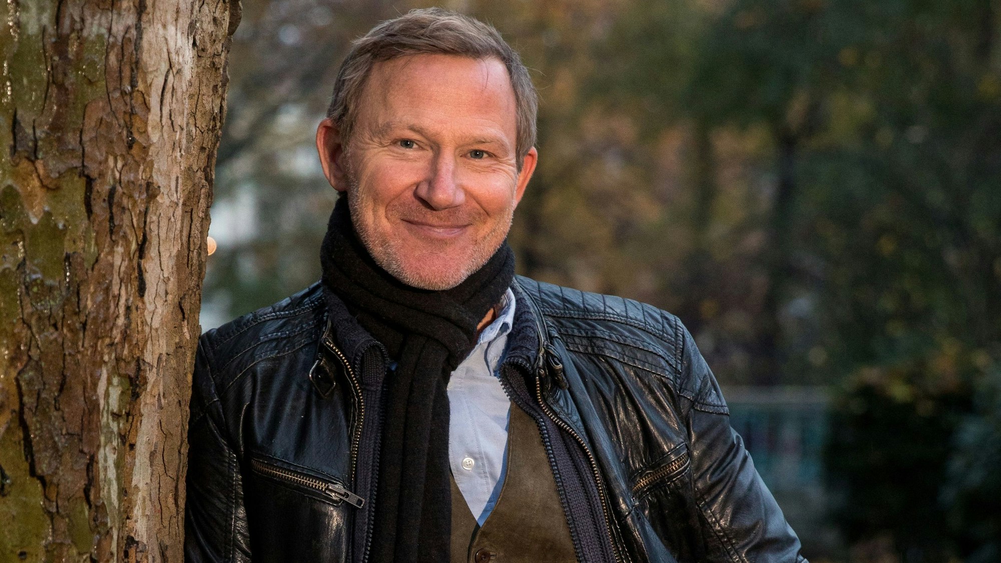 Schauspieler Roland Jankowsky mit Schal und Lederjacke an einen Baum gelehnt