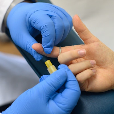 Hände mit Schutzhandschuhen entnehmen Blut an einem Zeigefinger.