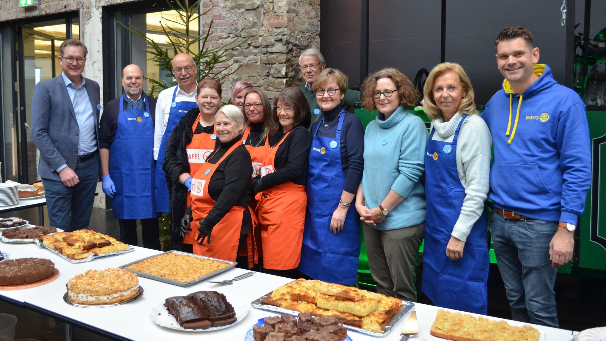 Mitglieder der Rotarier und der Tafel stehen vor einem Kuchenbuffet.