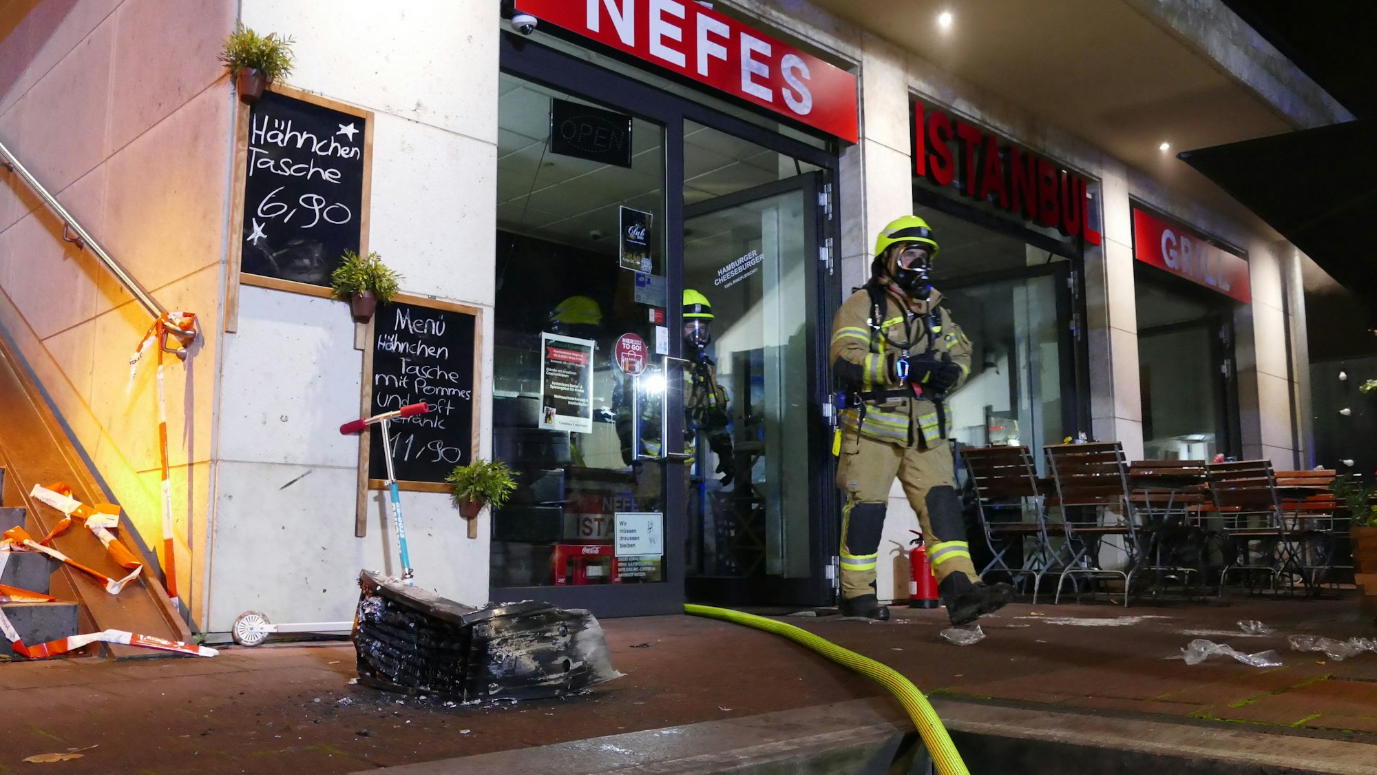 Zwei Feuerwehrmänner mit Atemschutzmaske kommen aus dem Imbiss, in dem es zu dem Brand kam.