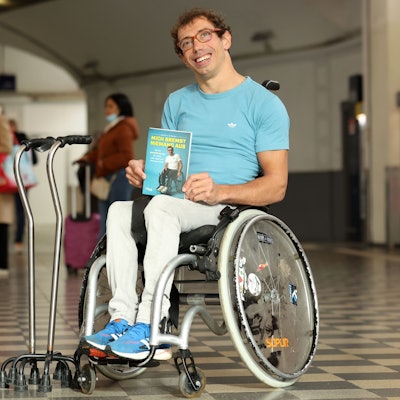 Johannes Grasser sitzt in seinem Rollstuhl und hält sein Buch „Mich bremst niemand“ aus in seinen Händen.