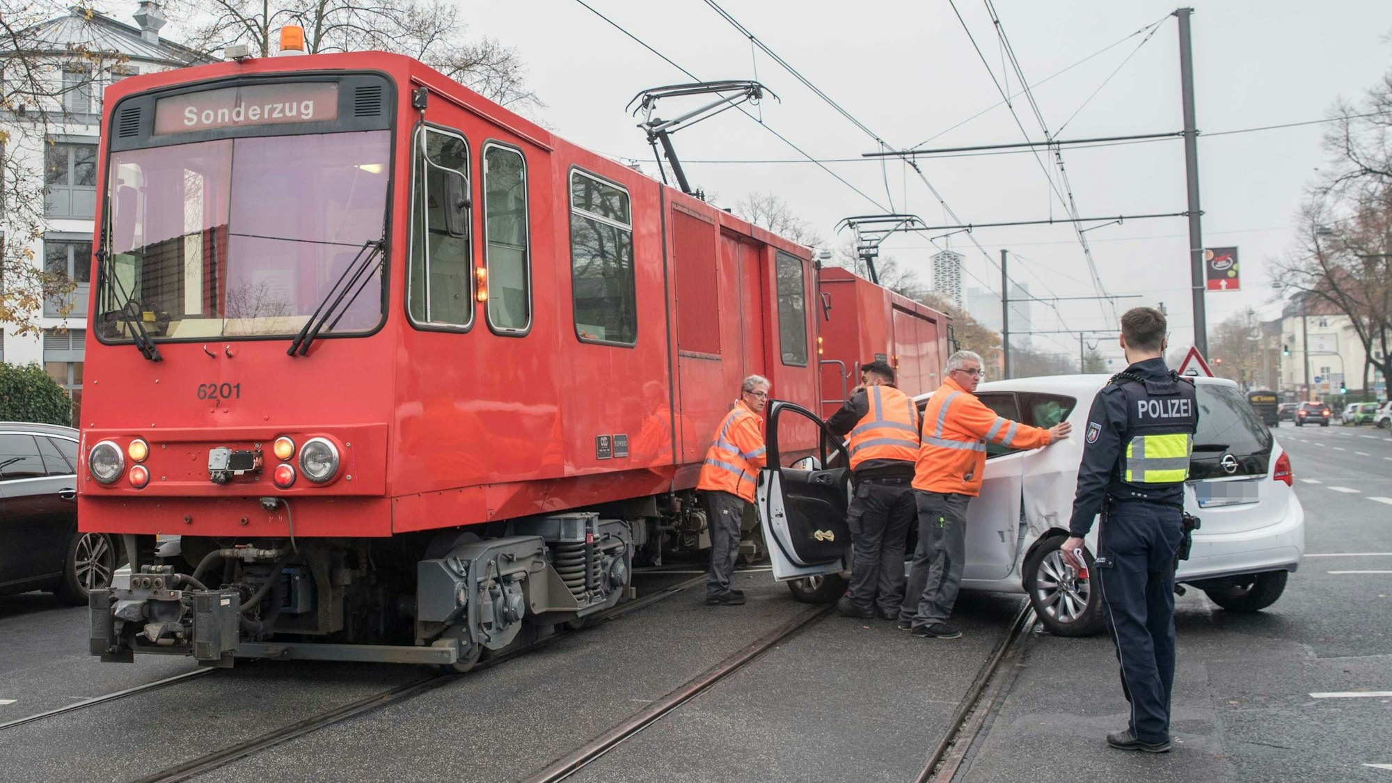Ein Auto ist seitlich gegen die KVB-Bahn gefahren. KVB-Mitarbeiter und ein Polizist sehen davor.