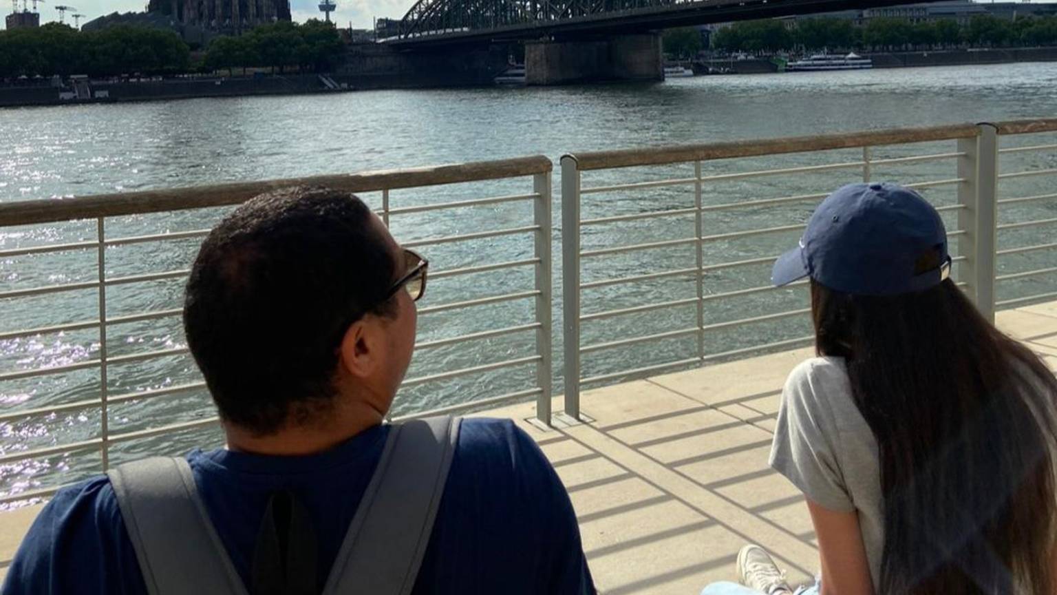 Zwei geflüchtete Jugendliche sitzen am Rhein und blicken auf den Kölner Dom.