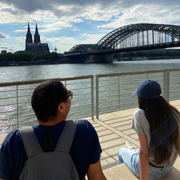 Zwei geflüchtete Jugendliche sitzen am Rhein und blicken auf den Kölner Dom.