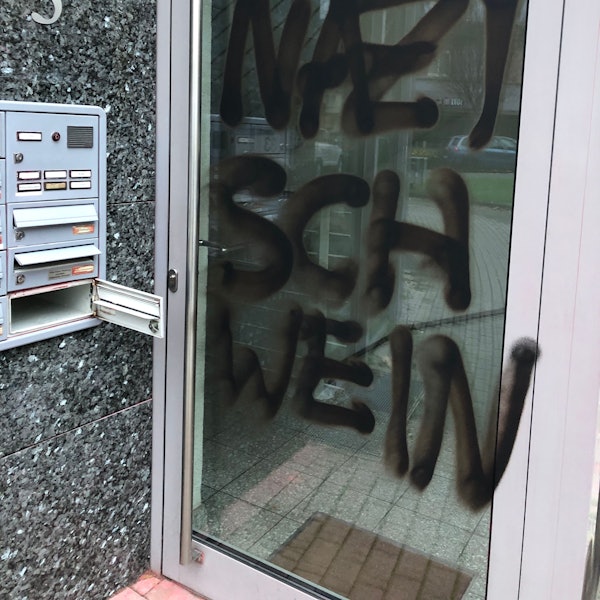 Eine Bürotür, darauf zu sehen in schwarzer Farbe: der Schriftzug „Nazischwein“.