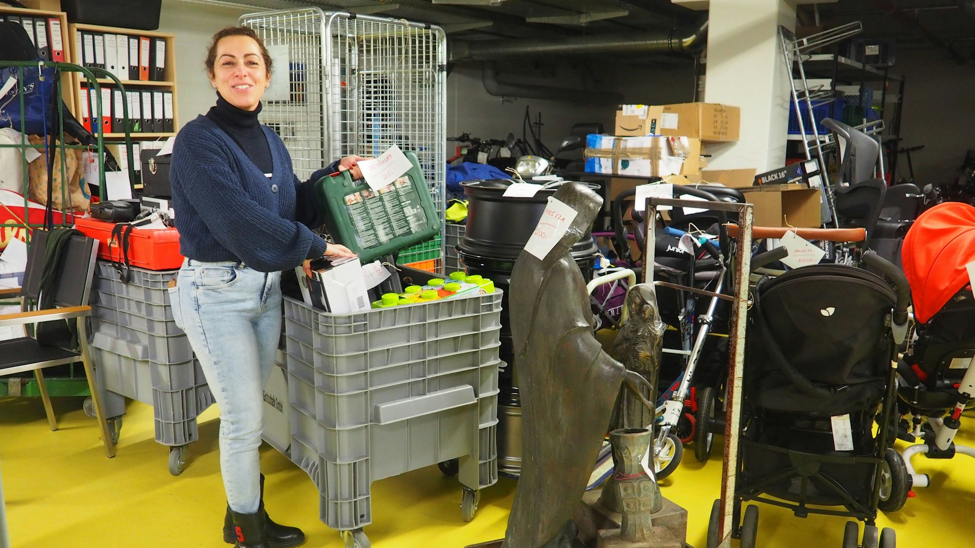 Selma Sacco steht in blauer Strickjacke zwischen Kisten voller Fundsachen.