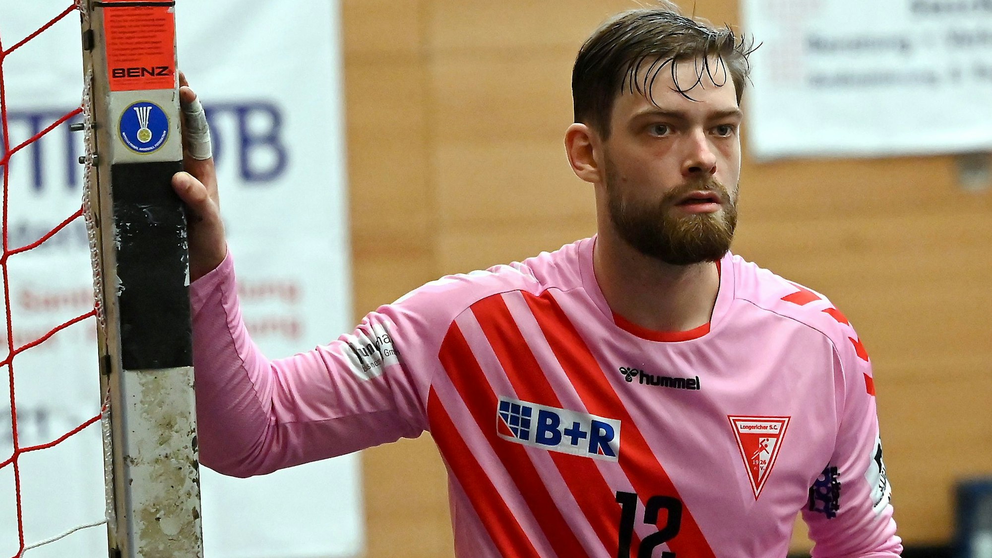 Ein Handballtorwart blickt aufs Spielfeld und hält sich mit dem rechten Arm am Pfosten fest.