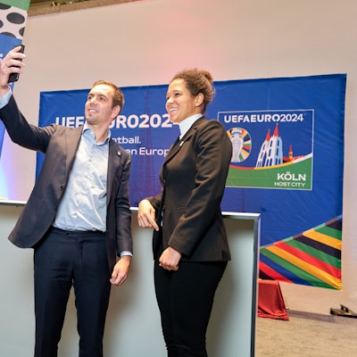 Der Fußballer Philipp Lahm steht links neben Celia Šašić. In seiner ausgestreckten Hand hält er ein Smartphone, um ein Selfie zu machen.