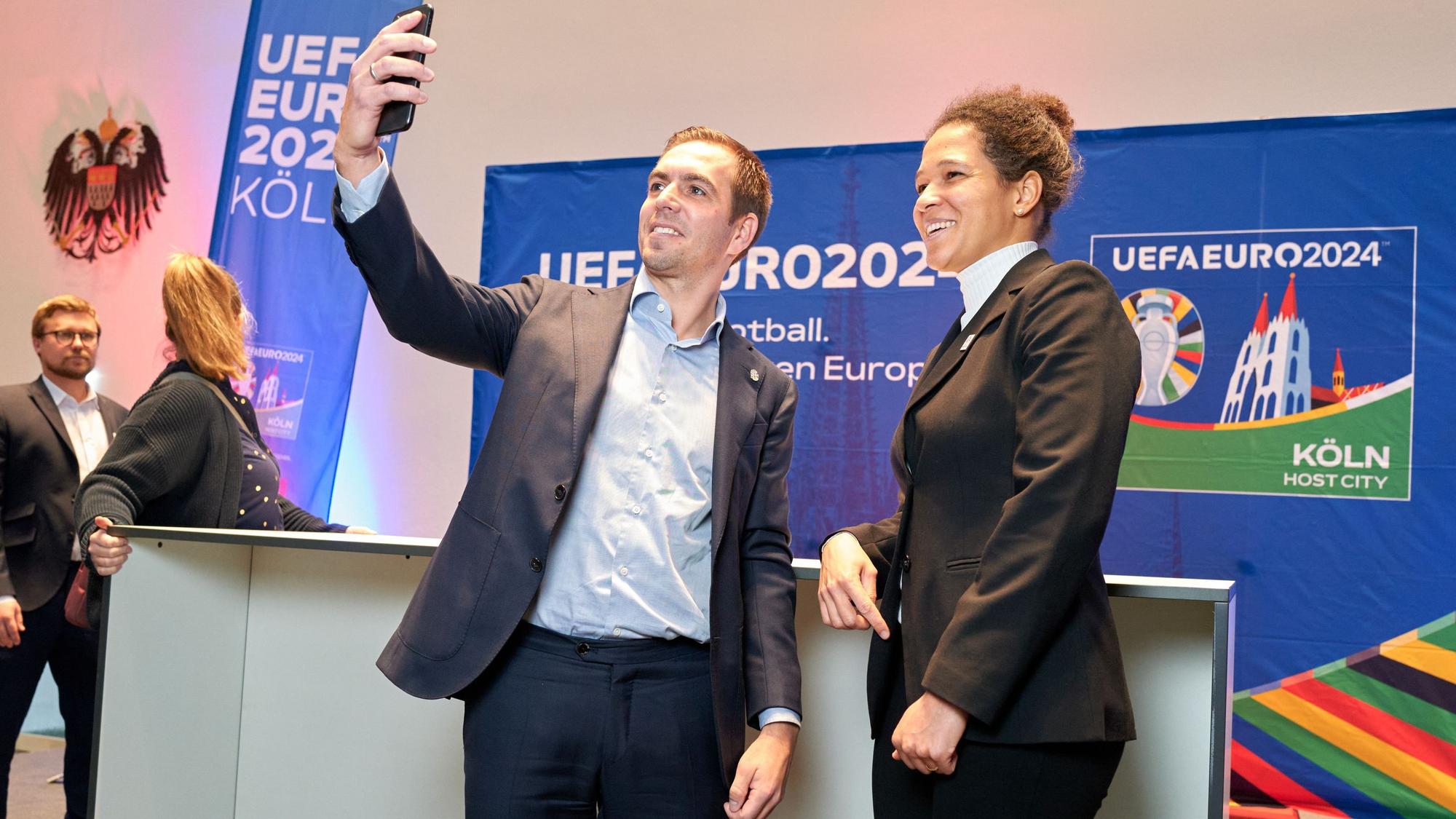 Der Fußballer Philipp Lahm steht links neben Celia Šašić. In seiner ausgestreckten Hand hält er ein Smartphone, um ein Selfie zu machen.