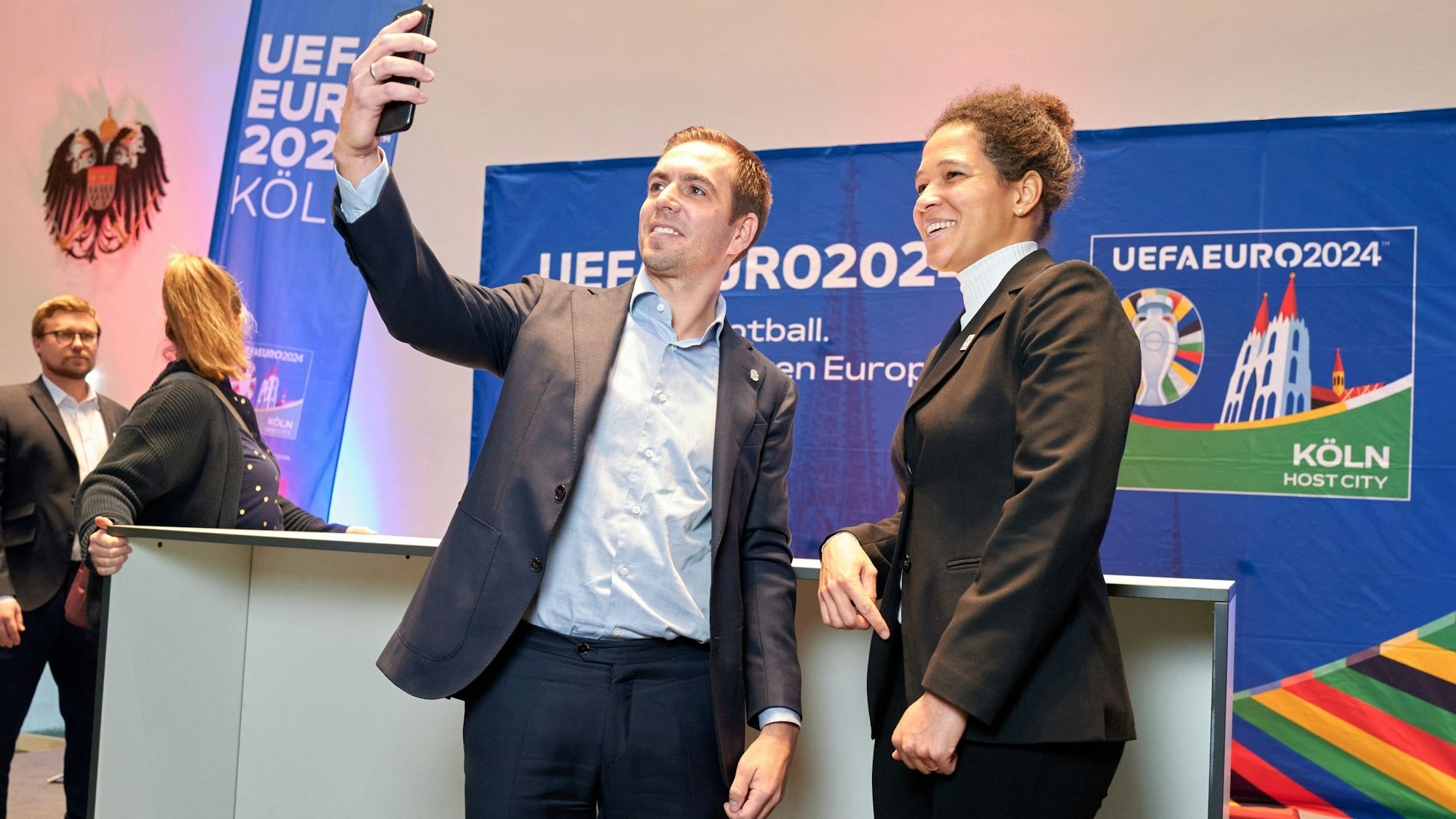 Der Fußballer Philipp Lahm steht links neben Celia Šašić. In seiner ausgestreckten Hand hält er ein Smartphone, um ein Selfie zu machen.