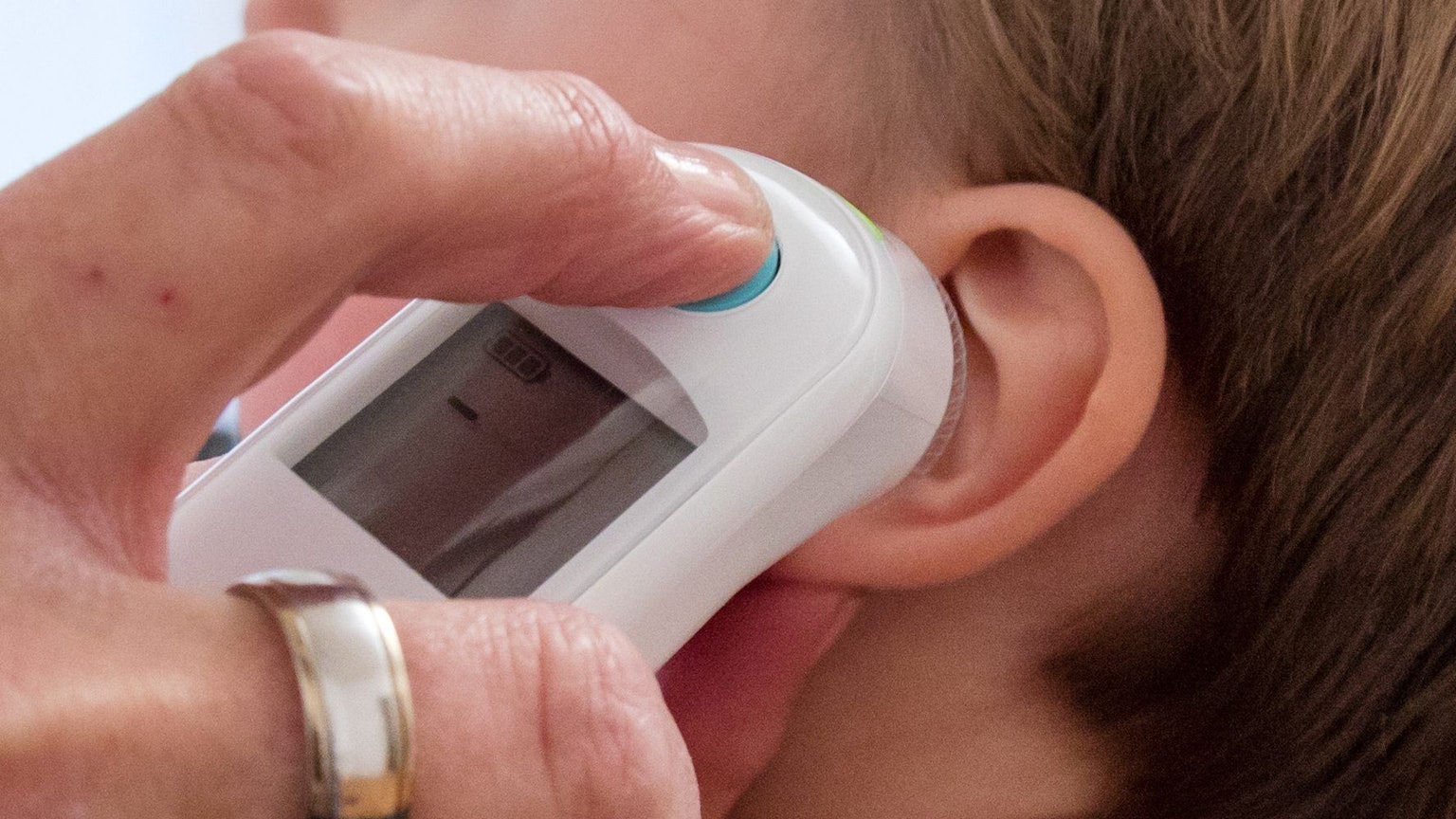 Hand mit Fieberthermometer am Ohr eines Kleinkindes.