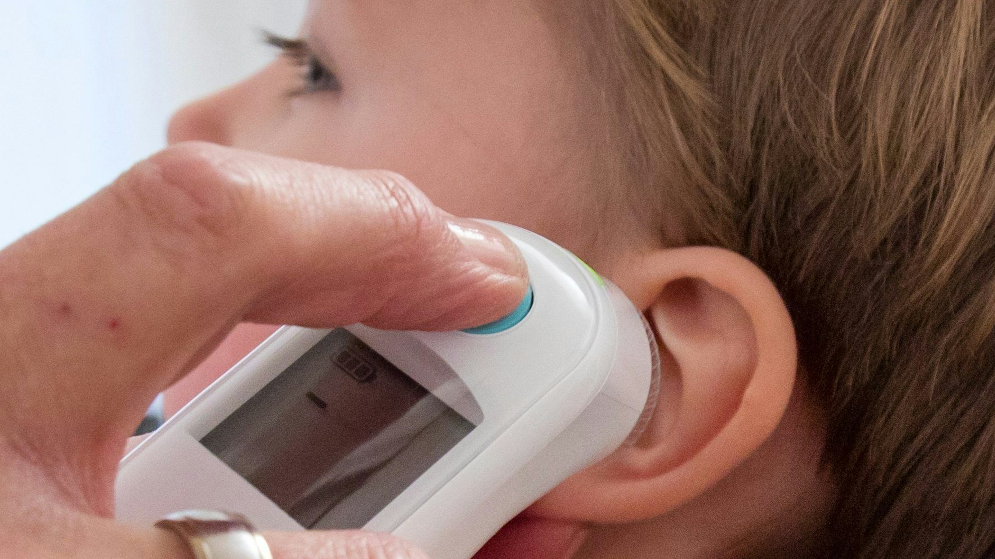 Hand mit Fieberthermometer am Ohr eines Kleinkindes.