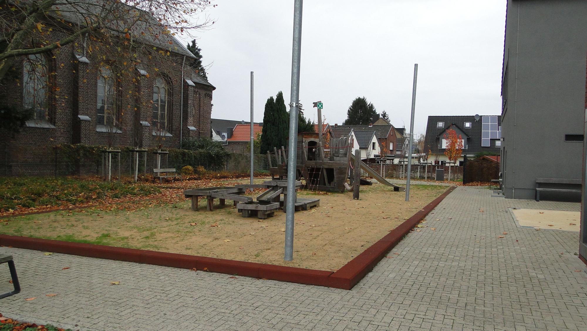 Spielgerüste stehen auf einem Hof, im Hintergrund sind Häuser, links daneben ein Schulgebäude.