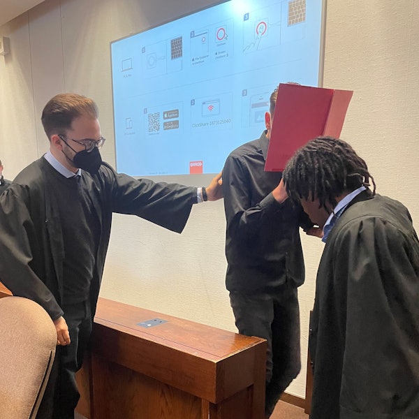 Der Angeklagte beim Prozessauftakt im Landgericht mit seinen Verteidigern Maximilian Klefenz und Dawit Stefanos. Der Angeklagte versteckt sein Gesicht hinter einem Aktenordner.