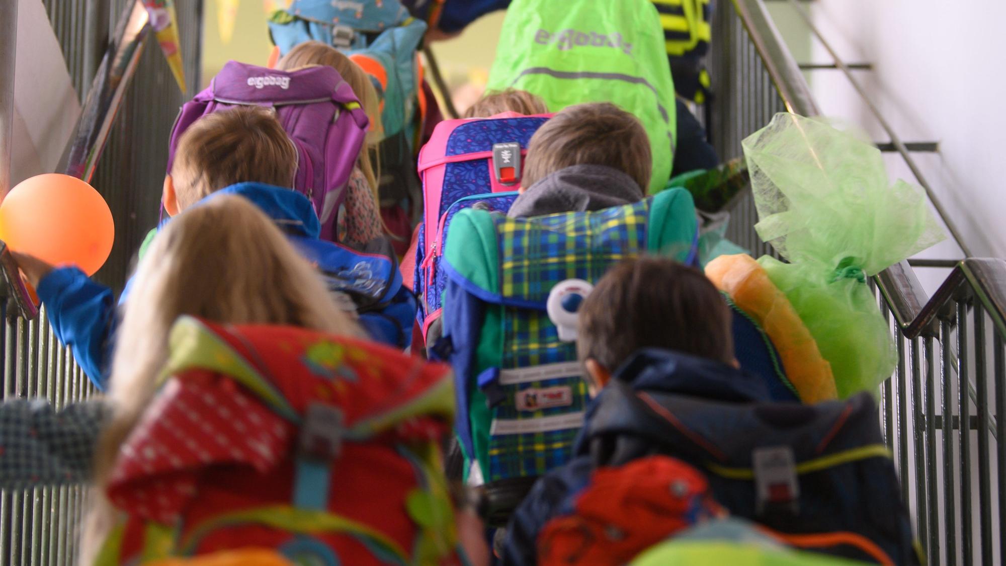 Auf dem Bild sind Kinder mit Schulranzen von hinten zu sehen. Sie gehen eine Treppe hinauf. (Symbolbild)