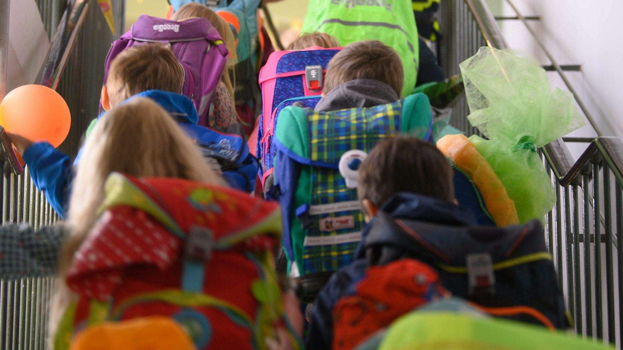 Kinder mit Ranzen gehen eine Schultreppe hoch.