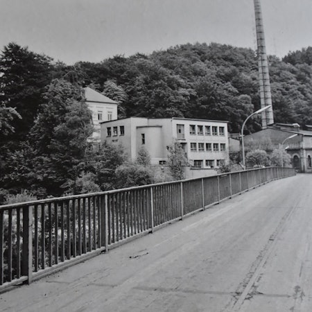 Ein Bild in schwarzweiß zeigt eine Brücke und mehrere Gebäude.