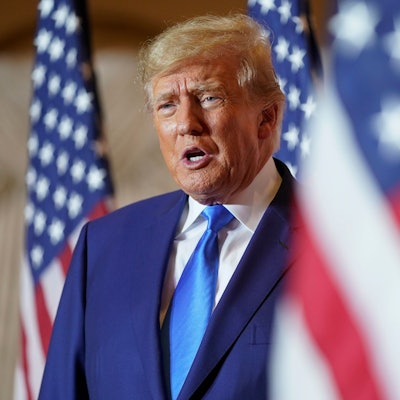 Es ist Trump zu sehen, der hinter einer US-amerikanischen Flagge steht.