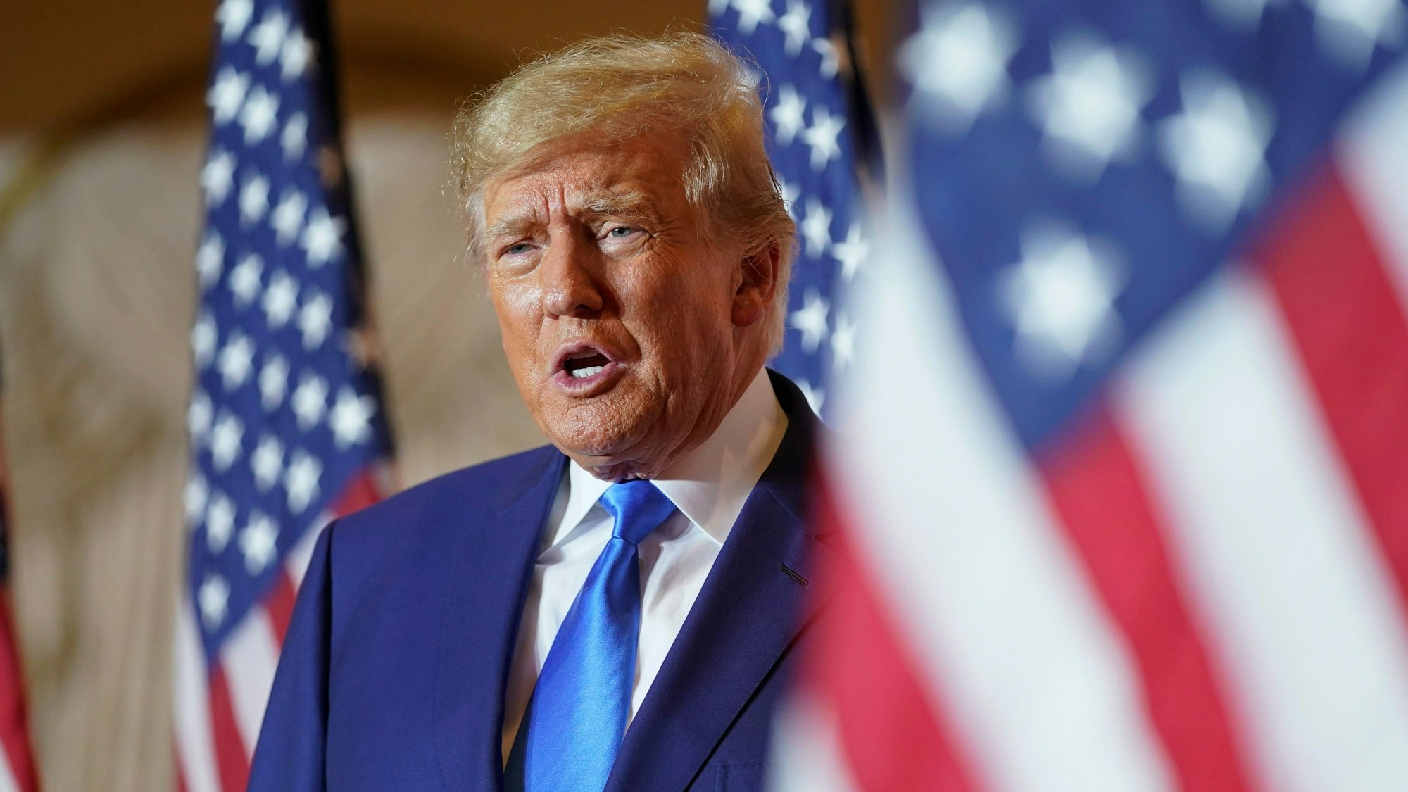 Es ist Trump zu sehen, der hinter einer US-amerikanischen Flagge steht.