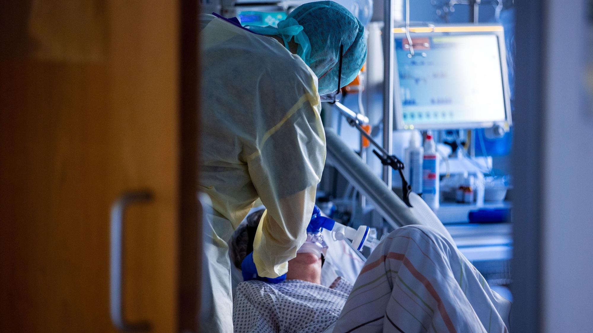 Ein Pfleger kümmert sich in Schutzausrüstung um eine Patientin, die beatmet wird.