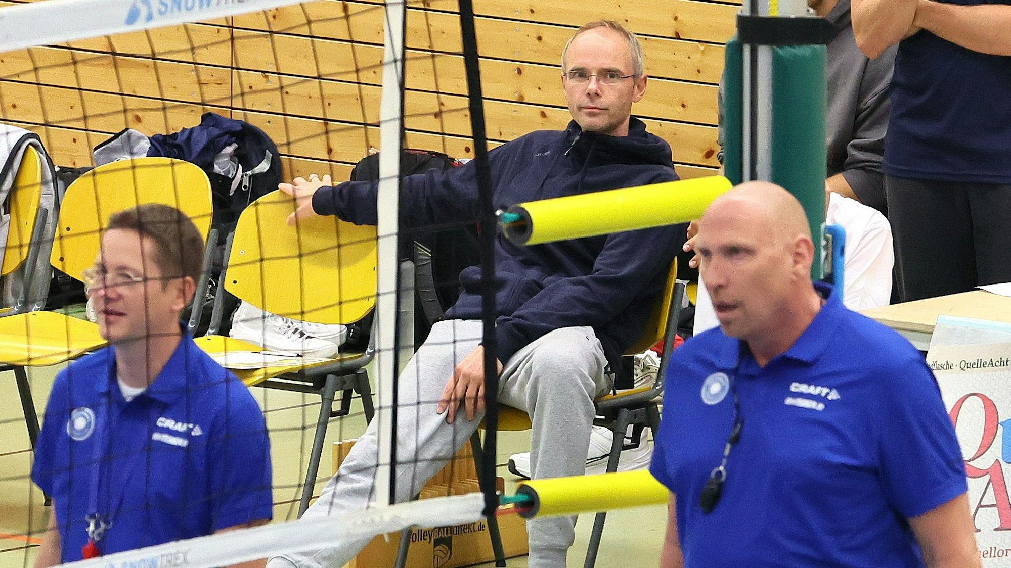 Ein Volleyball-Trainer sitzt auf einem Stuhl und schaut aufs Spielfeld.