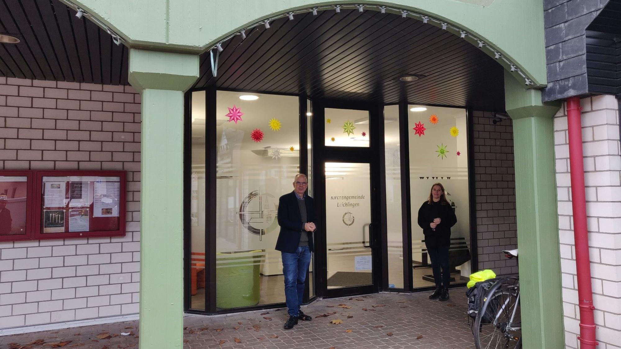 Presbyter Jens Weber und Büromitarbeiterin Doris Eret stehen vor dem Eingang des neuen evangelischen Gemeindebüros in den Arkaden in der Marktstraße 7.
