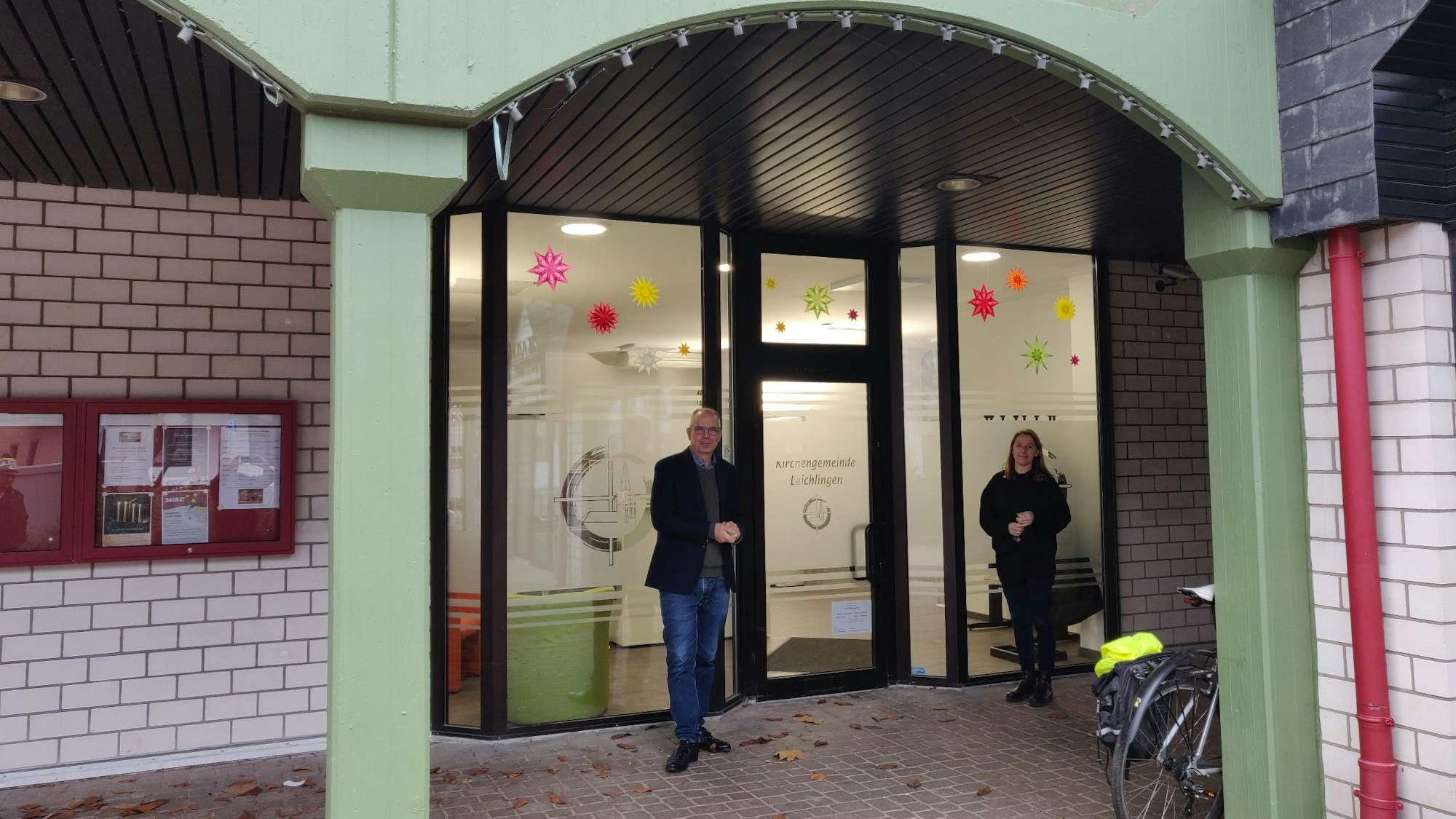 Presbyter Jens Weber und Büromitarbeiterin Doris Eret stehen vor dem Eingang des neuen evangelischen Gemeindebüros in den Arkaden in der Marktstraße 7.