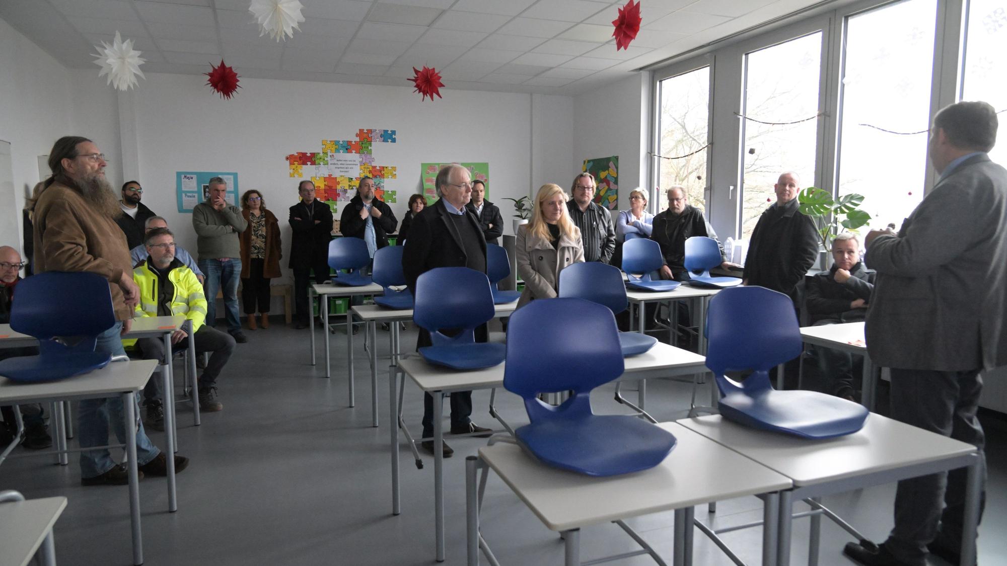 In einem Klassenraum stehen die Gäste der Führung durch das Rösrather Schulzentrum und hören einem Referenten zu.