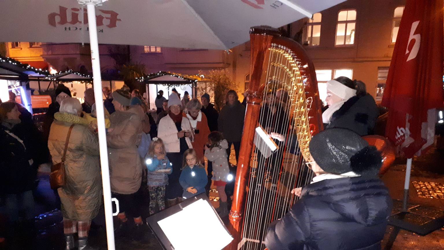 Eine Frau spielt auf der Harfe, Erwachsene und Kinder sehen ihr zu. Im Hintergrund ist auch der Nikolaus zu sehen.
