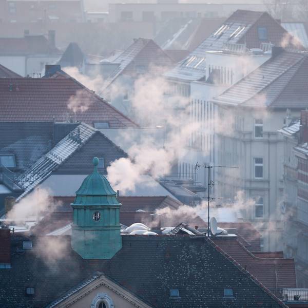 Die Dächer einer Siedlung im Winter, aus den Schornsteinen strömt Gas.