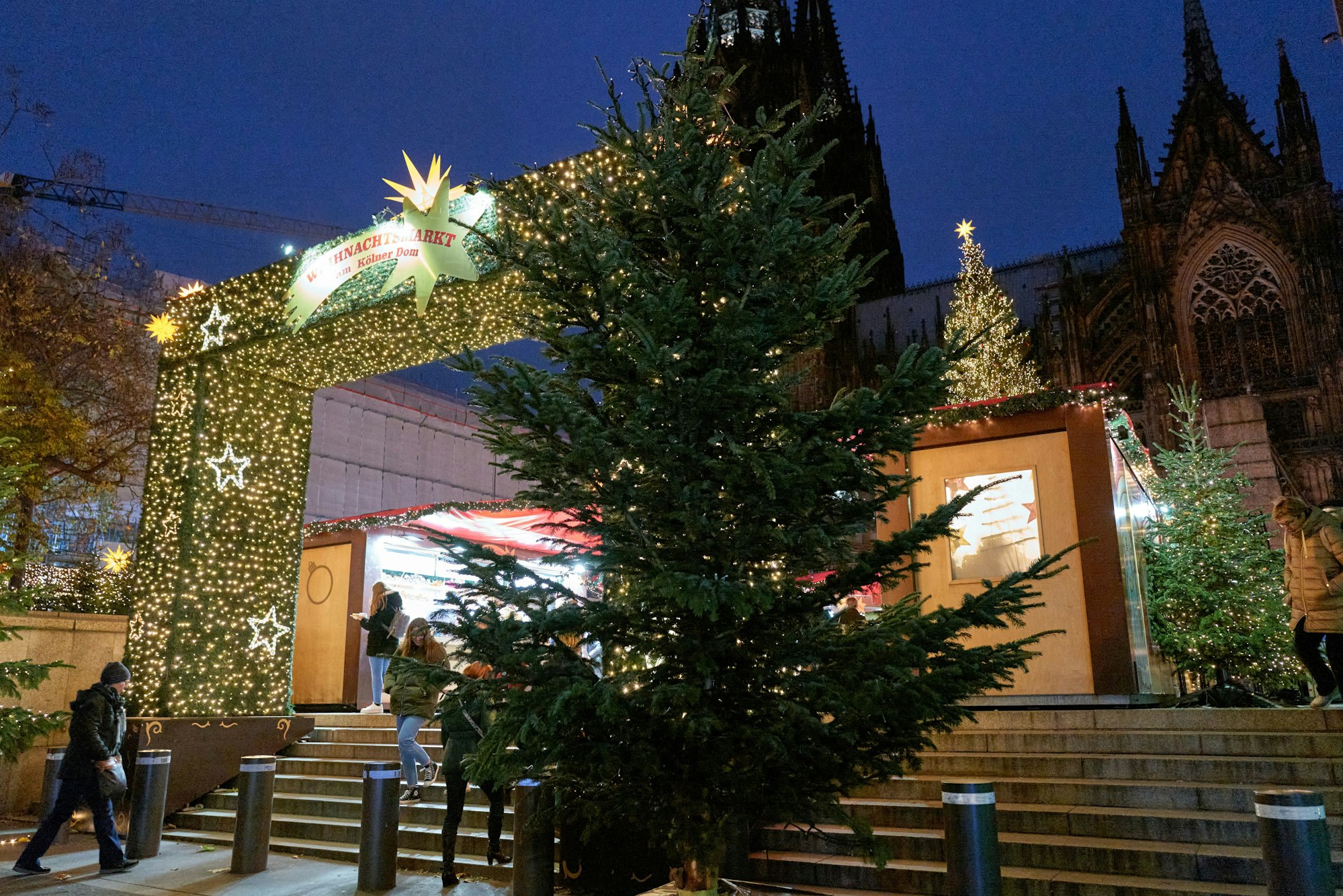 Ein hell erleuchteter Bogen ist der Eingang zum Weihnachtsmarkt auf der Domplatte. Davor steht ein Weihnachtsbaum.