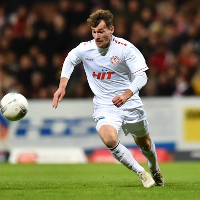Ein Fußballspieler läuft über den Platz und hat den Ball vor sich im Blick.
