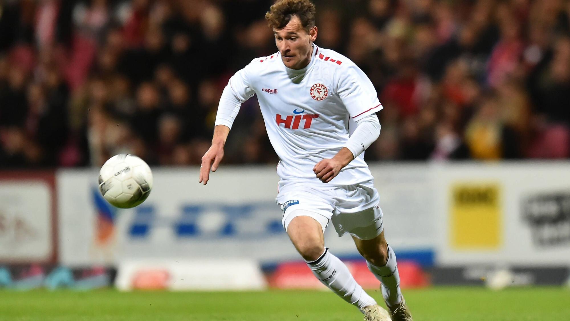 Ein Fußballspieler läuft über den Platz und hat den Ball vor sich im Blick.