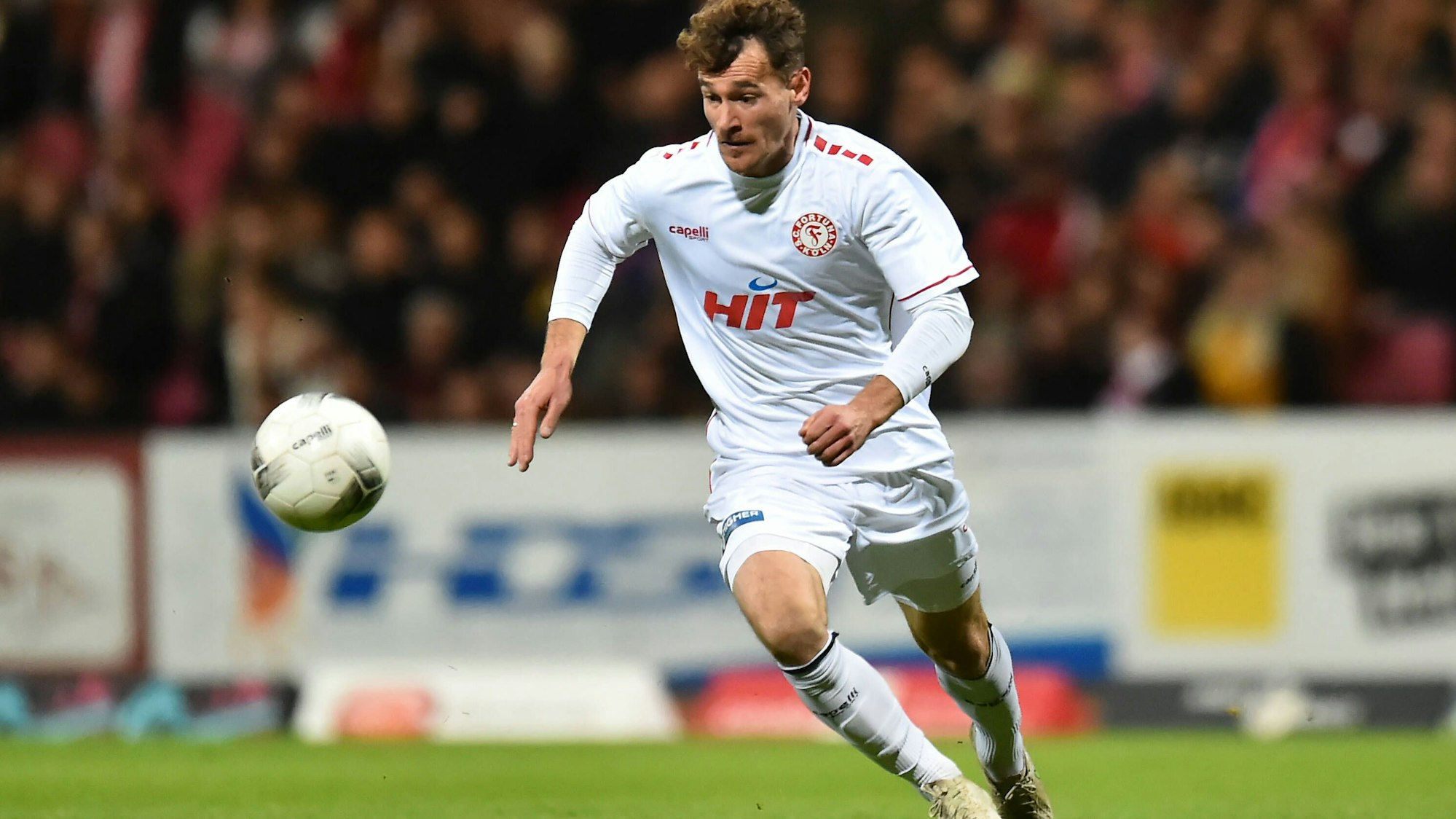 Ein Fußballspieler läuft über den Platz und hat den Ball vor sich im Blick.